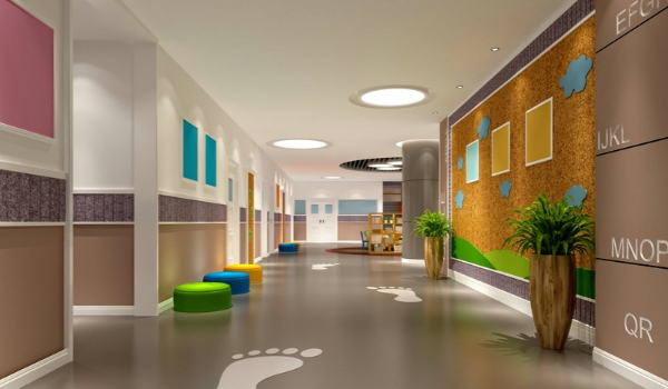 **Alt text:**  A bright, modern school or daycare hallway featuring colorful ottomans, potted plants, cork display boards on the walls, and white footprint decals marked along the floor.