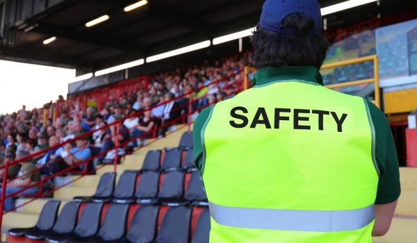 stadium steward with the phosphorescent jacket and the SAFETY writing who controls the fans in the packed stands
