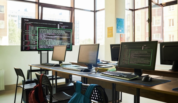 Empty classroom with multiple computer workstations displaying programming code on monitors