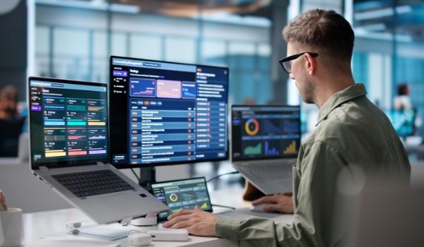 Alt text: A man reviews data dashboards on multiple screens at a desk.