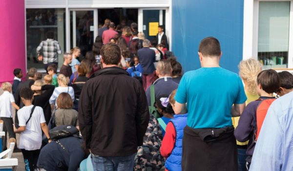 Students and adults gather outside a school entrance as a crowd moves through the open doors.