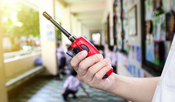 A man holding a red radio communication or handheld walkie-talkie at school