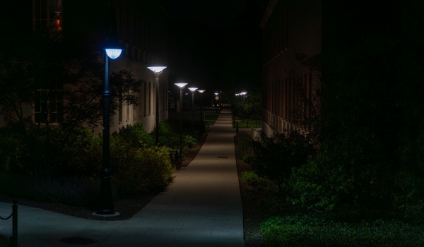 Serene university campus pathway at night, illuminated by a row of modern LED streetlights casting soft light on the sidewalk