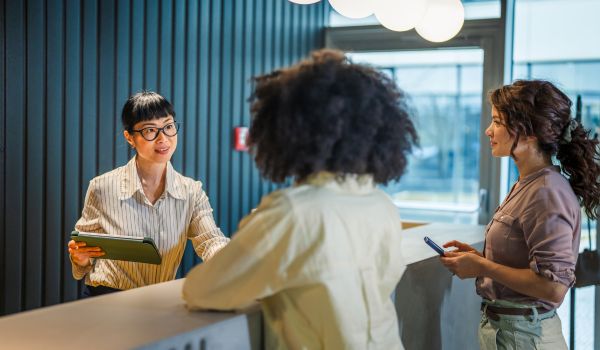 Receptionist assisting visitors at an office front desk.