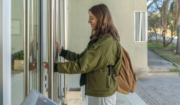 Smiling young woman opening glass door of office building