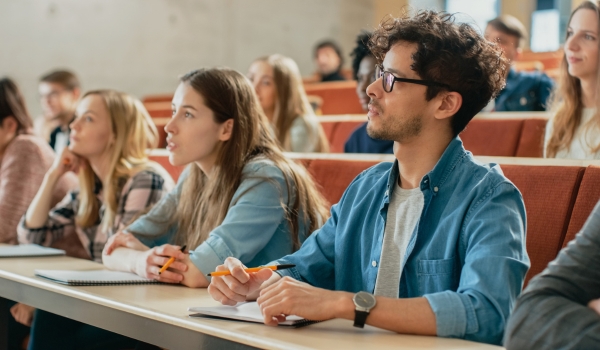 In the Classroom Multi Ethnic Students Listening to a Lecturer and Writing in Notebooks