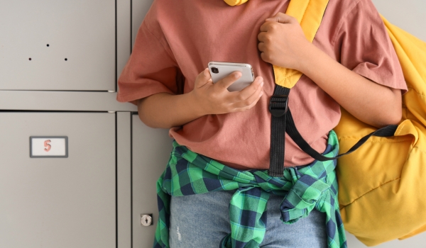 Teenage African-American schoolboy using mobile phone near locker, closeup
