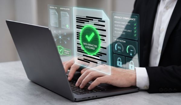 Person typing on a laptop with a digital overlay showing a redacted document, a green check mark and privacy compliance indicators.