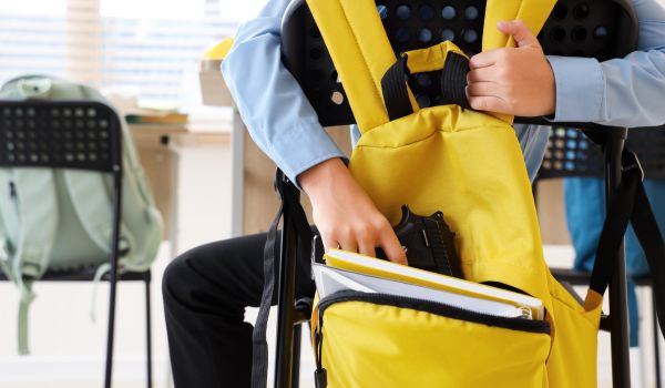 Boy taking gun from backpack in classroom, closeup