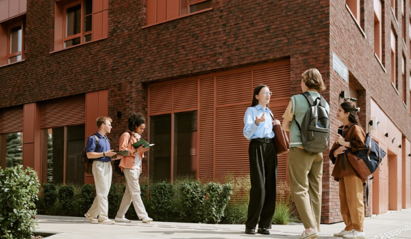A group of university students chatting and walking together outside a modern brick campus building.