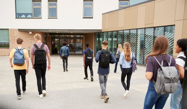 Rear View Of High School Students Walking Into College Building Together