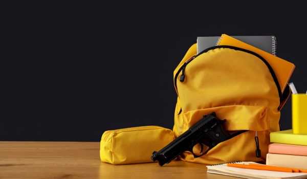 Backpack with gun and books on table against dark background
