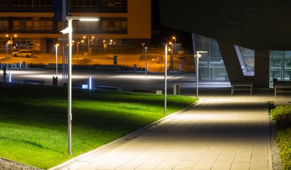 Streetlights illuminate a paved campus walkway and surrounding lawns at night.