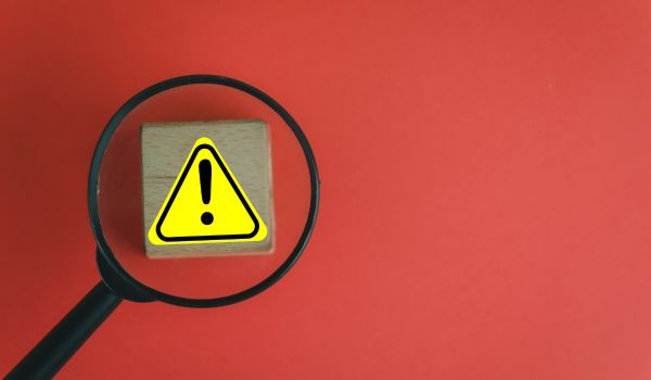 A magnifying glass inspecting a warning symbol on a block